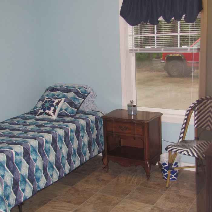 A simple bedroom with a single bed, nightstand, and a window overlooking outside.