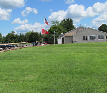 A building with flags and a large green lawn under a cloudy sky.