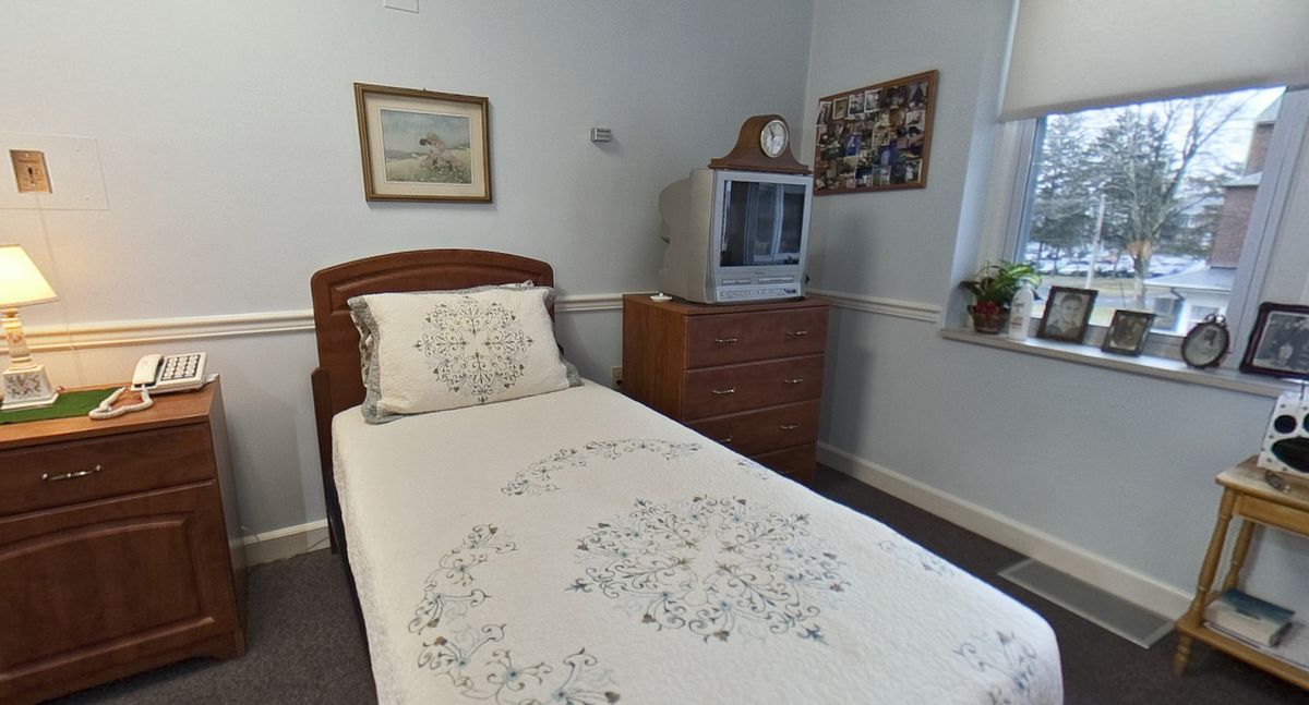 A cozy bedroom with a single bed, floral bedspread, and a TV on a wooden dresser.