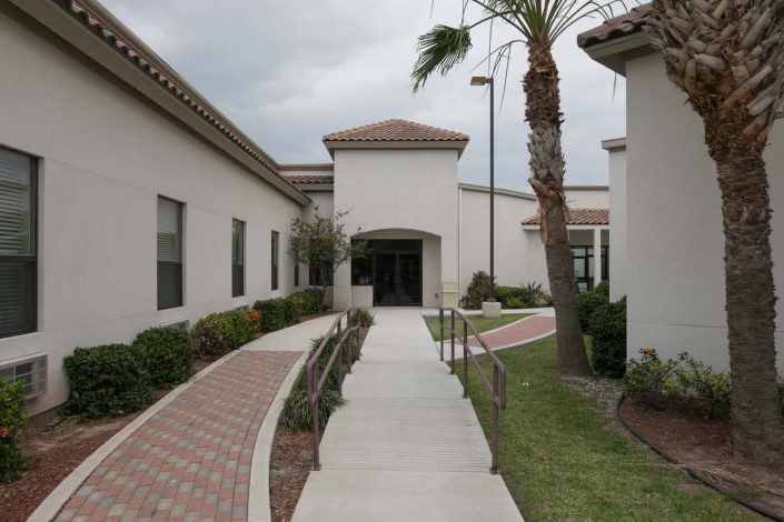 A modern building with a landscaped pathway and palm trees leading to the entrance.