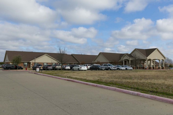 A wide view of a building with a parking lot filled with vehicles under a partly cloudy sky.