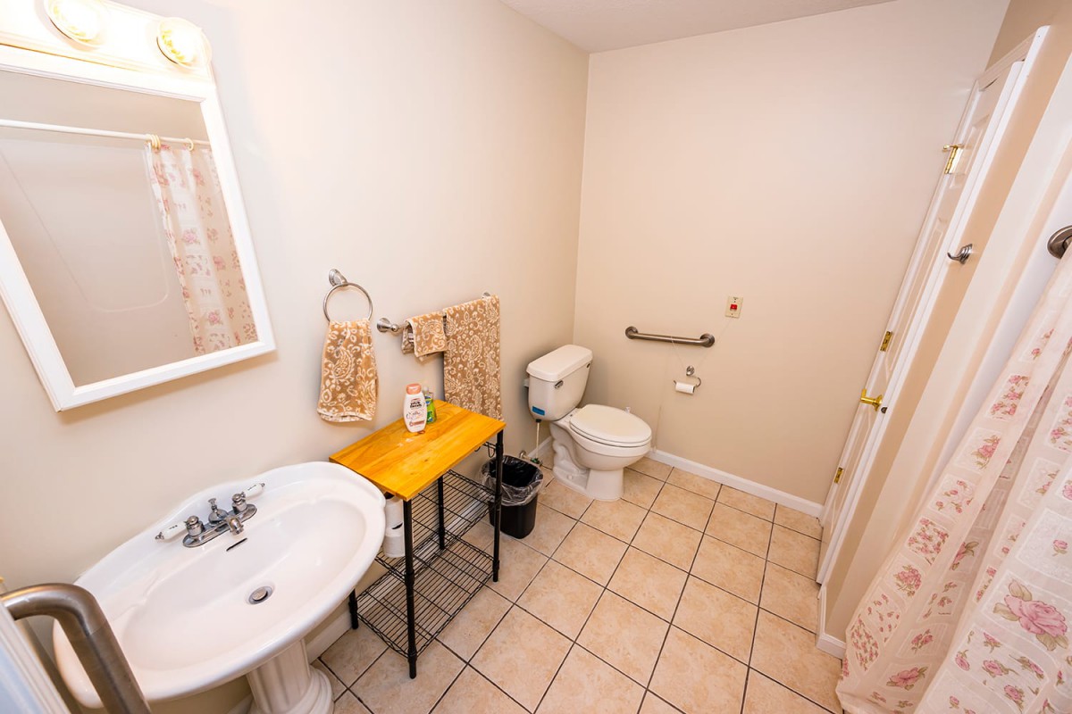 A well-organized bathroom featuring a sink, toilet, and handrail on tile flooring.