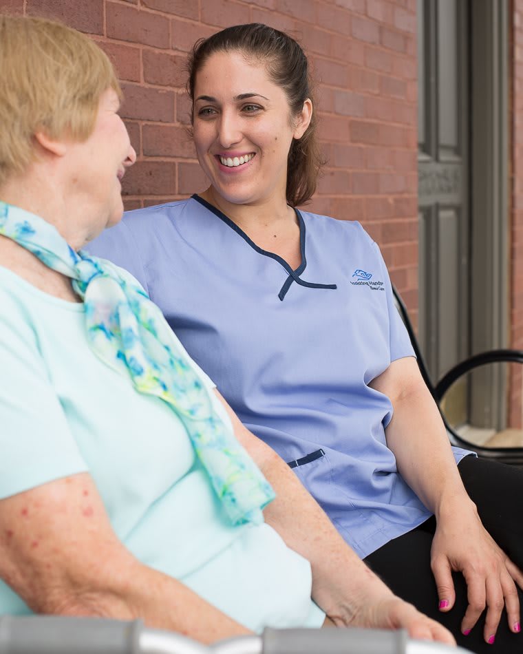A nurse and an elderly woman smiling and conversing outdoors.