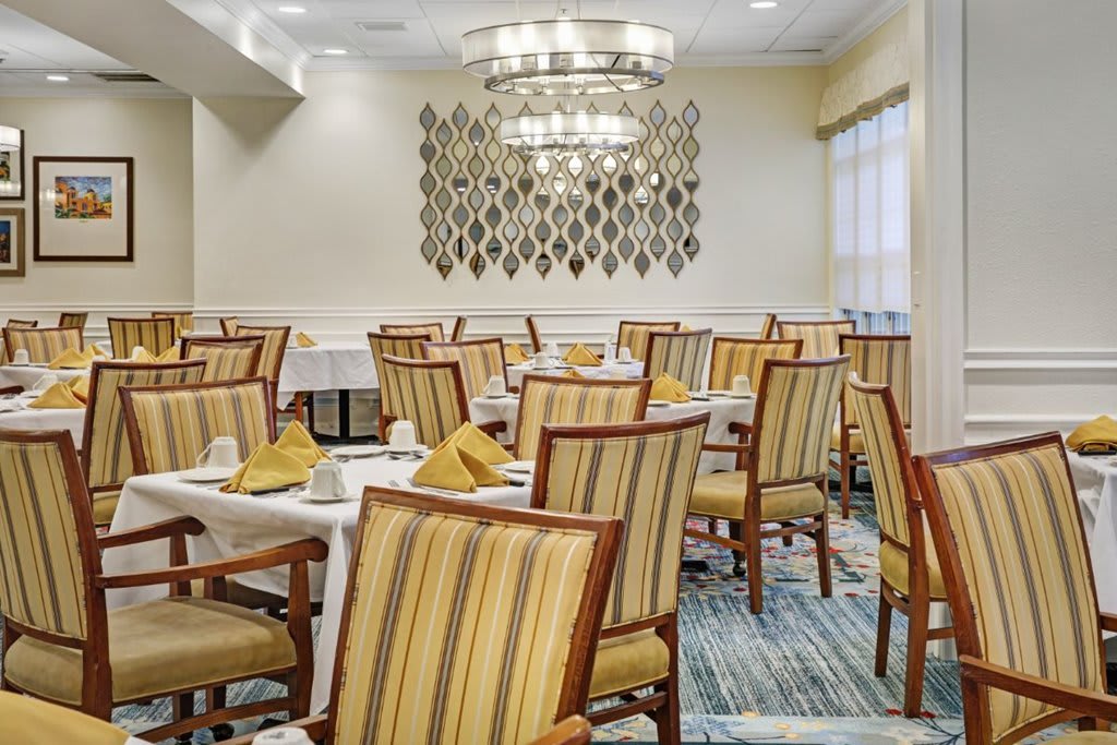 A well-lit dining area with neatly arranged tables and chairs, featuring an elegant chandelier.