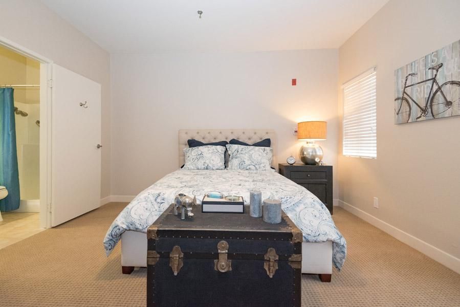 A cozy bedroom featuring a neatly made bed, a lamp on the nightstand, and a decorative trunk at the foot of the bed.