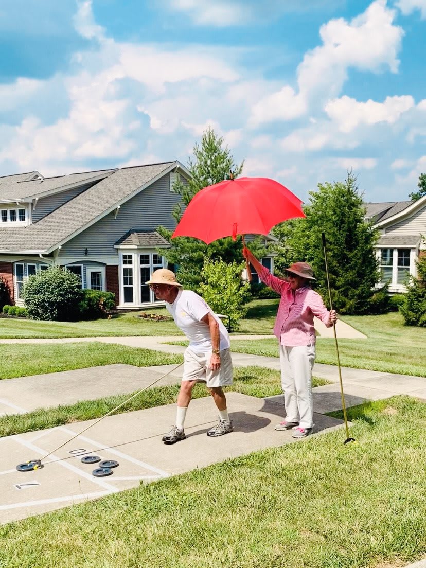 Two people walking on a sunny day, one holding a red umbrella.