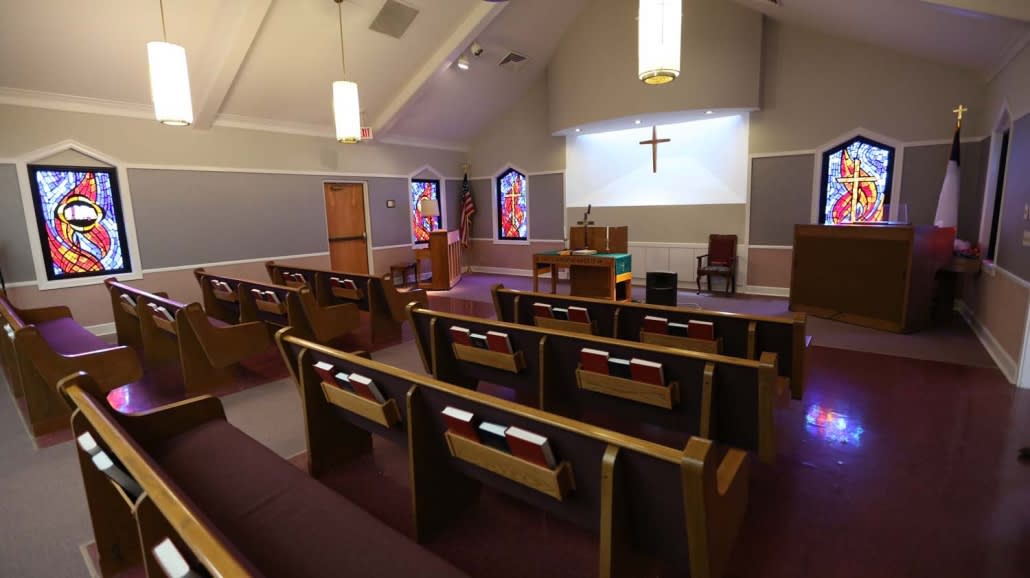 A peaceful church interior with pews, an altar, and stained glass windows.