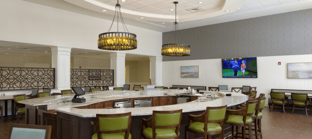 A modern kitchen bar area with pendant lighting and green upholstered chairs.