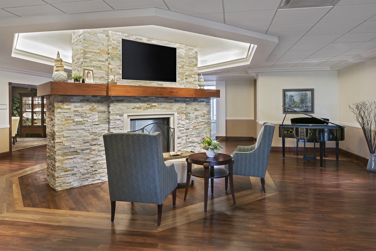 A cozy living room with a stone fireplace, armchairs, and a television mounted above.