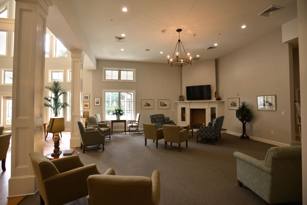 A spacious living room featuring comfortable seating, a fireplace, and a mounted TV, illuminated by natural light from large windows.
