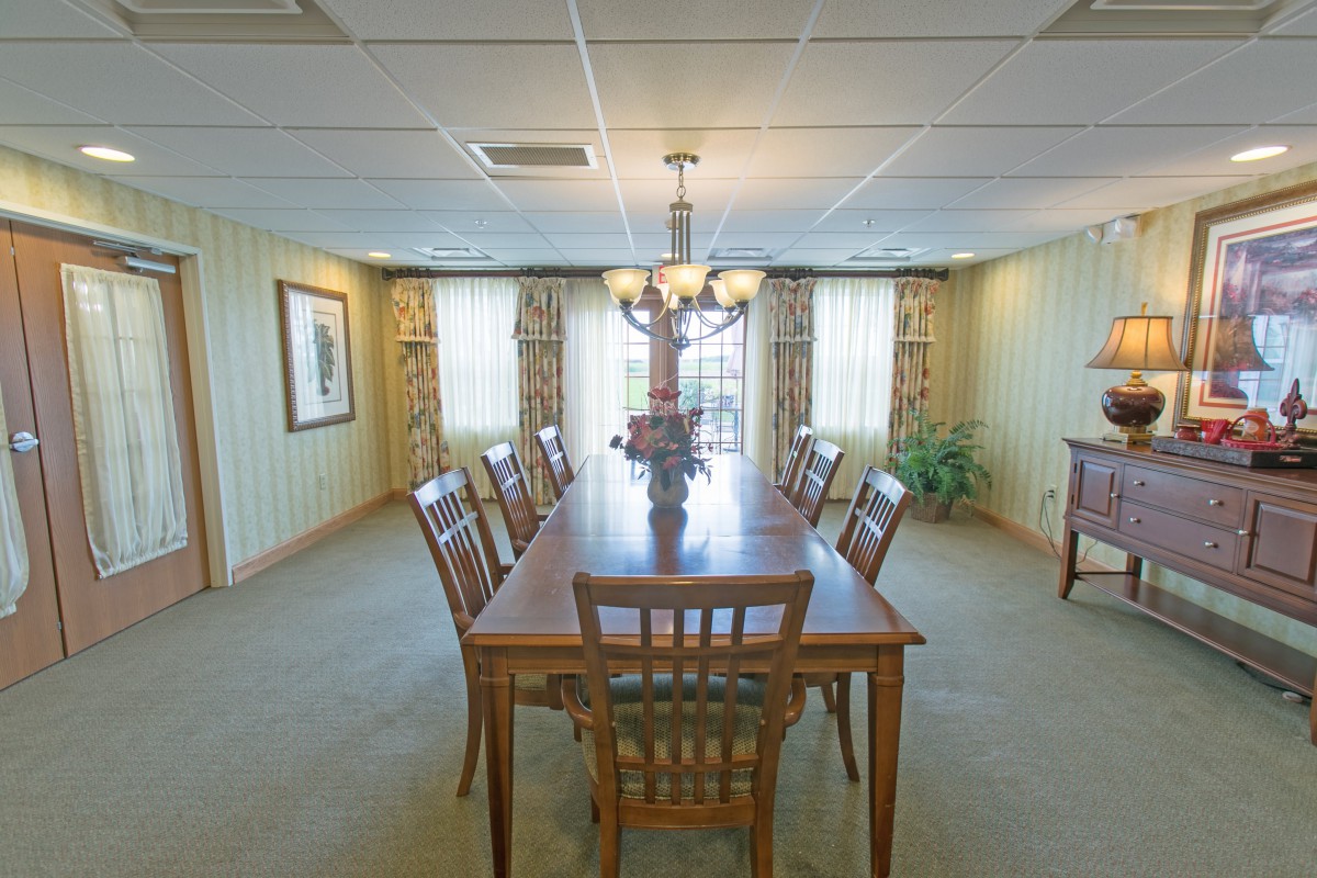 A spacious dining room with a long wooden table and matching chairs, illuminated by a chandelier.