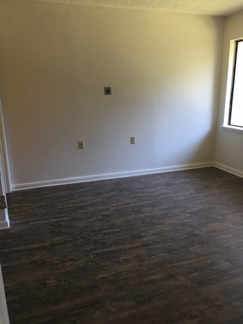 An empty room with wooden flooring and a large window.