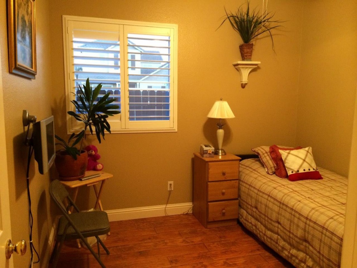 Cozy bedroom with a bed, nightstand, and plants by the window.