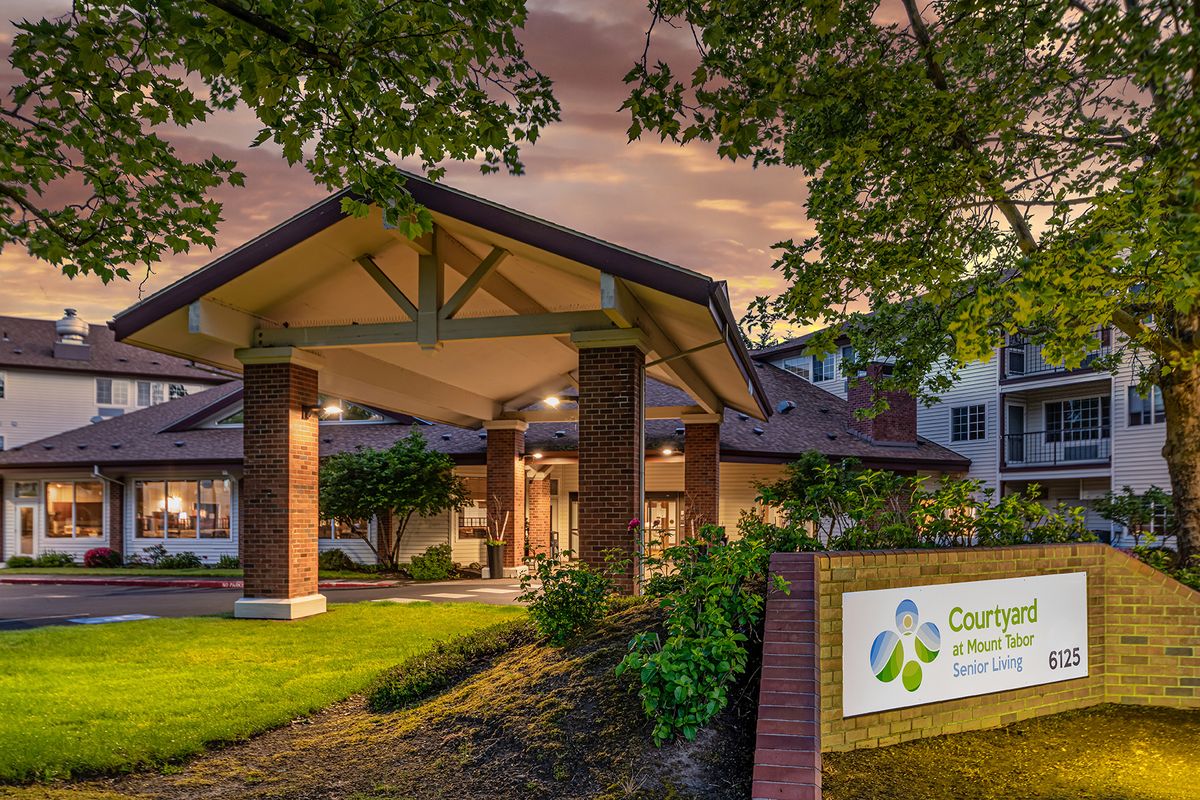 A welcoming entrance to a building with decorative landscaping and a prominent sign at dusk.