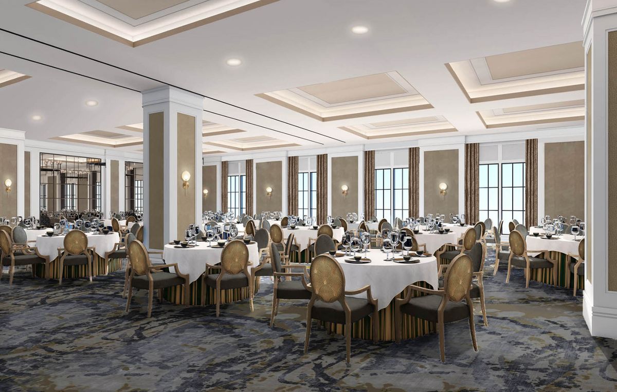 An elegantly set banquet hall ready for a formal event, featuring round tables with white tablecloths and decorative chairs.