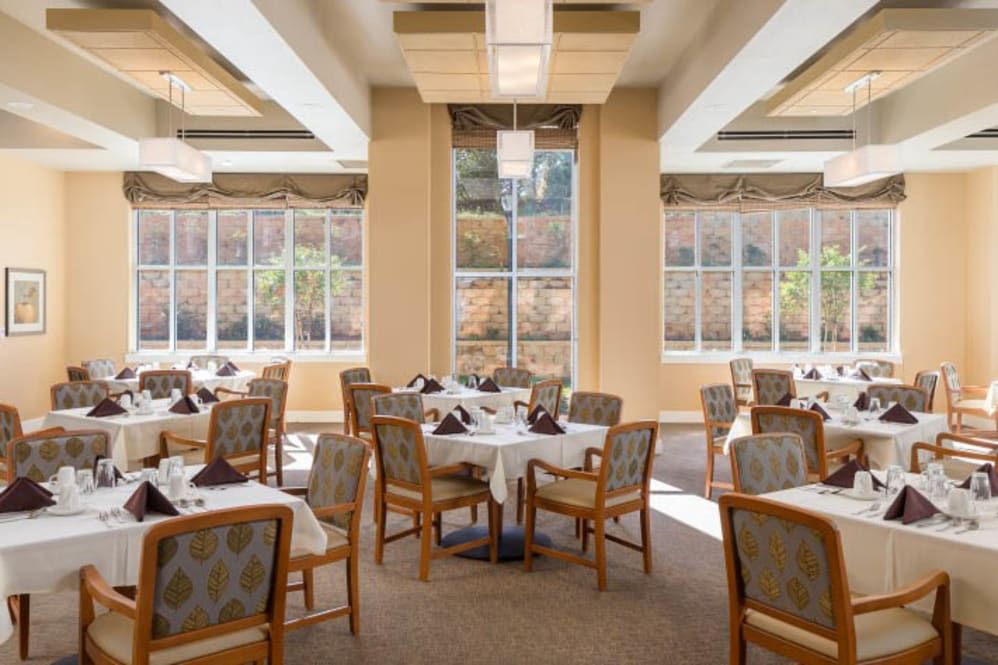 A bright and inviting dining area with neatly arranged tables and chairs, featuring large windows that allow natural light to fill the space.