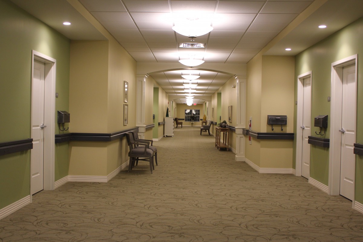 A well-lit hallway with carpeted flooring and chairs along the sides.