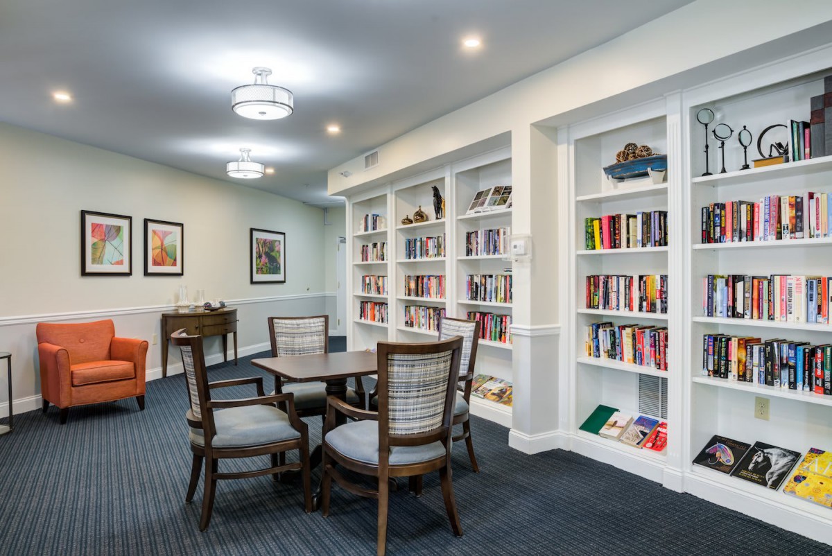 A cozy library with bookshelves, a table with chairs, and soft lighting.