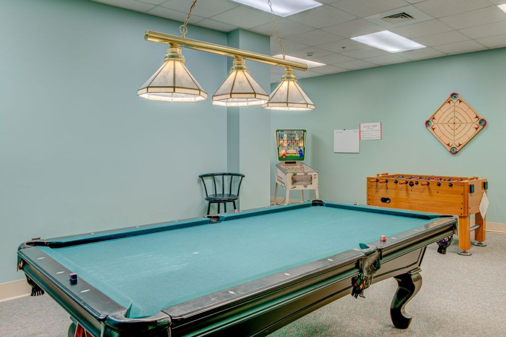 A game room featuring a large pool table with overhead lights, a chair in the corner, and decor on the walls.