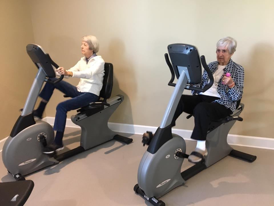 Two elderly individuals exercising on stationary bikes indoors.