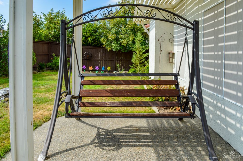 A garden swing with a wooden seat and metal frame on a patio.