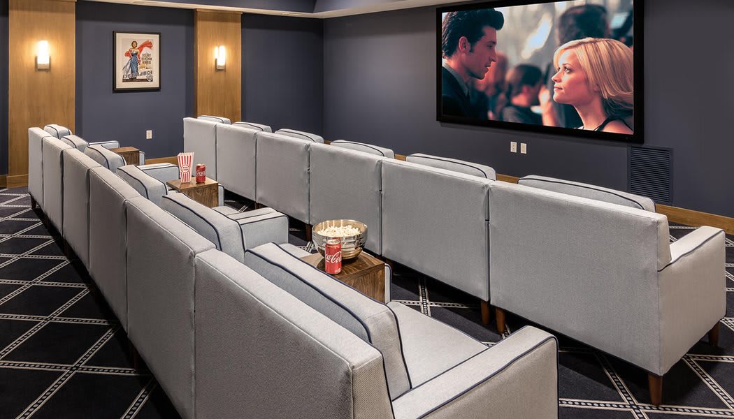 A modern home theater room with rows of comfortable couches and a large screen displaying a movie.