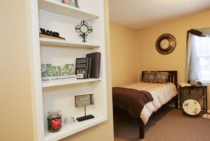 A cozy bedroom featuring a neatly arranged wall shelf and a bed with brown accents.