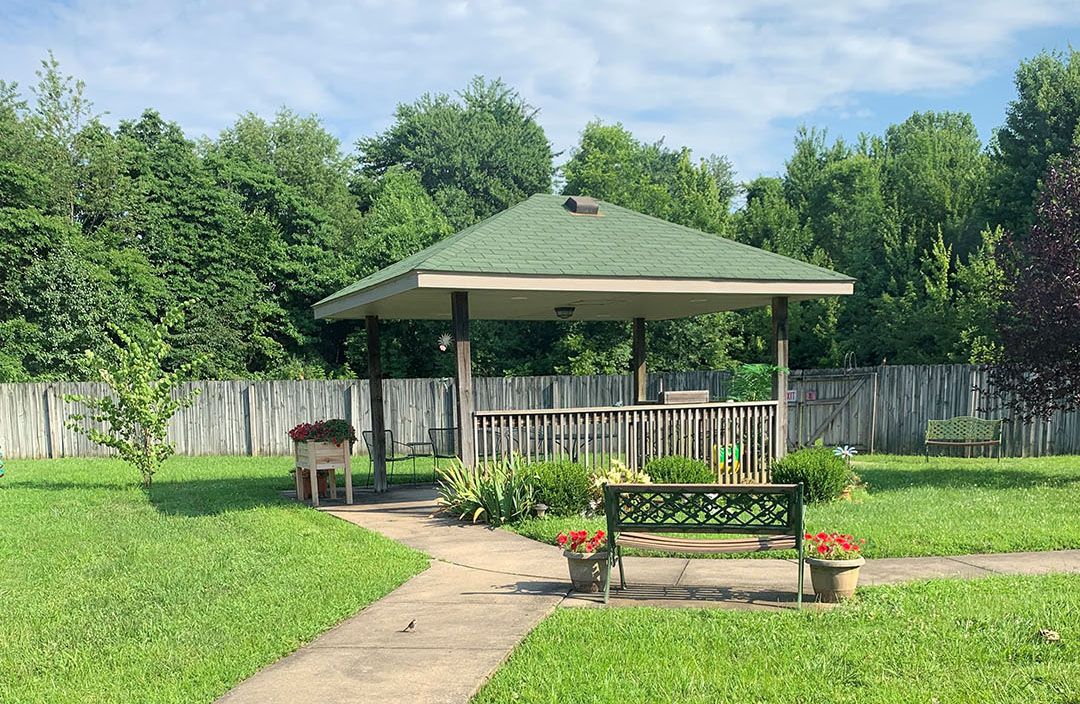 A peaceful garden setting with a gazebo, bench, and lush greenery.