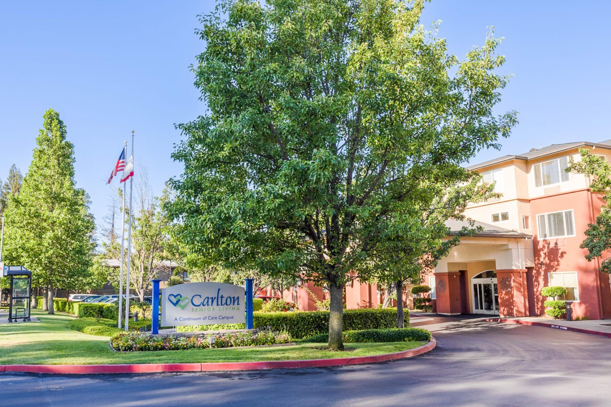 A sunny view of a building with a sign and flagpoles at the entrance.