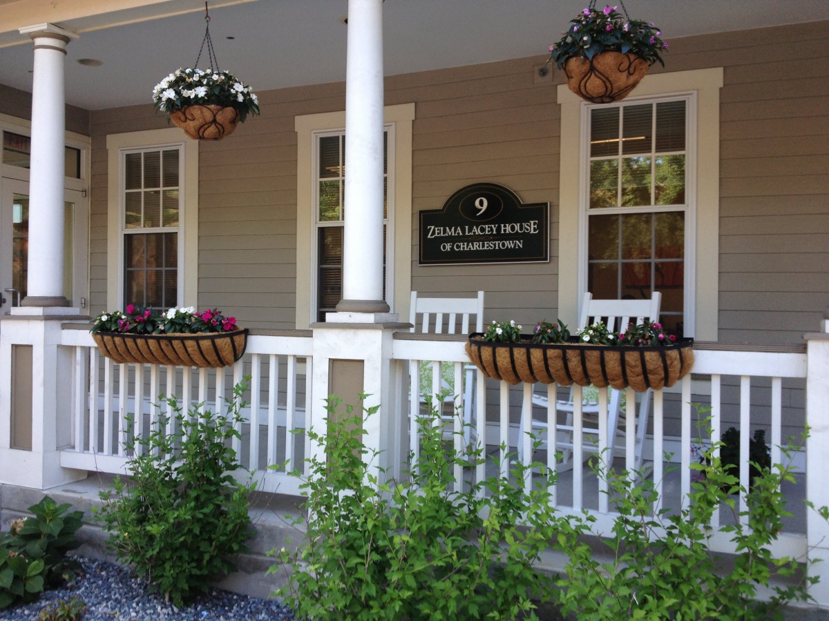 A cozy porch with hanging flower baskets, rocking chairs, and a welcoming sign.