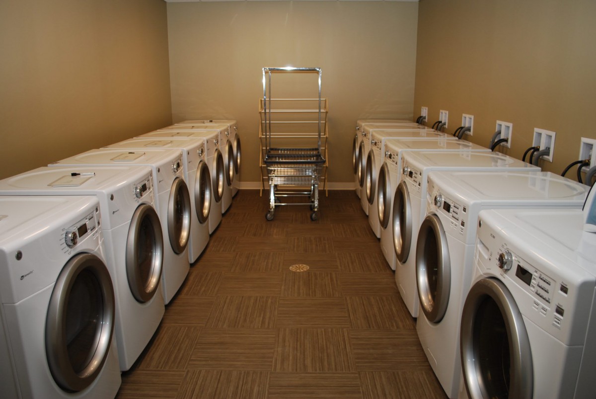 A laundry room with multiple washing machines lined up along the walls and a drying rack in the center.