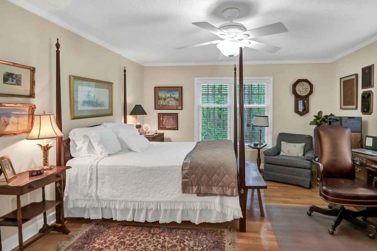 A cozy, traditional bedroom featuring a four-poster bed, armchair, and framed artwork.