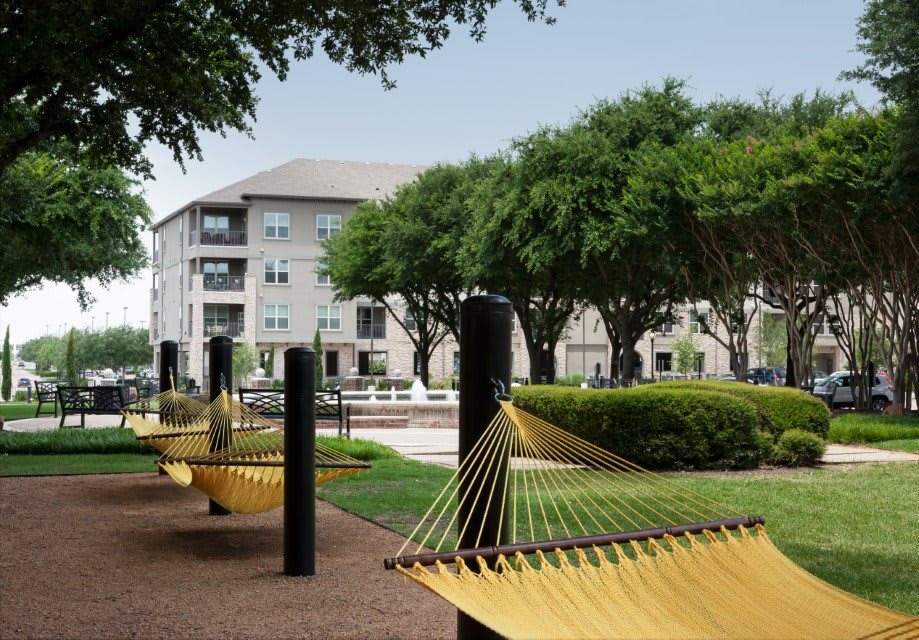 Outdoor area with hammocks and apartment buildings surrounded by trees.