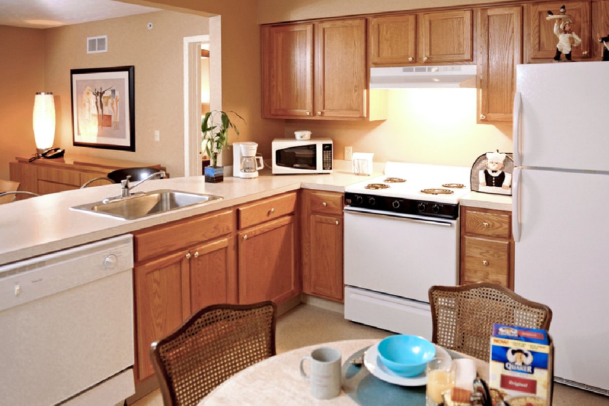 A cozy kitchen with wooden cabinets, featuring a microwave, stovetop, and dining table set.