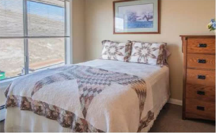 A cozy bedroom with a patterned quilt and artwork above the bed.