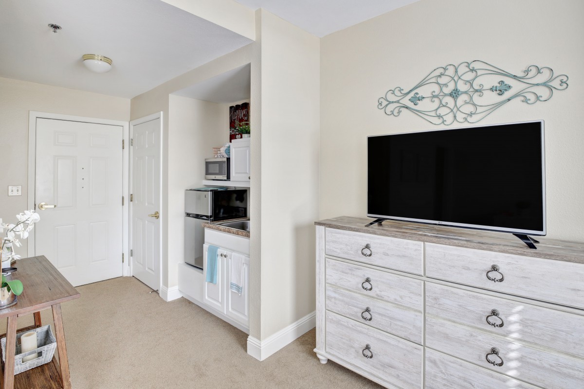 A modern bedroom with a dresser and television, featuring minimalist decor and white furniture.