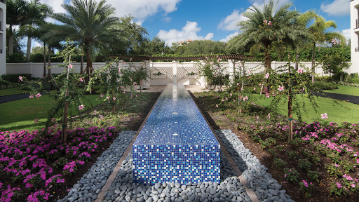 A serene garden featuring a striking blue mosaic water feature, surrounded by lush tropical plants and vibrant flowers.