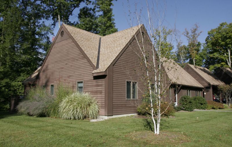 A wooden house surrounded by a landscaped yard with trees and grass.
