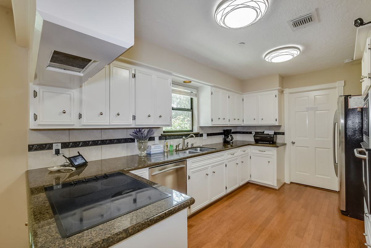 A modern kitchen with white cabinets, granite countertops, and wooden flooring.