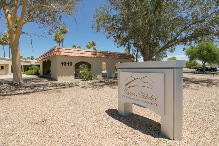 A desert landscape features a building with an archway and a sign in the foreground.