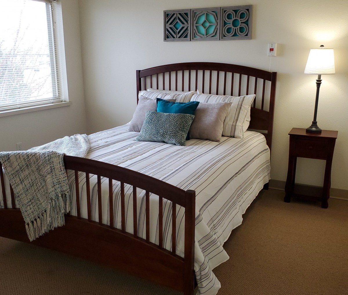A cozy and neatly arranged bedroom with a wooden bed, soft pillows, and a lamp on the bedside table.