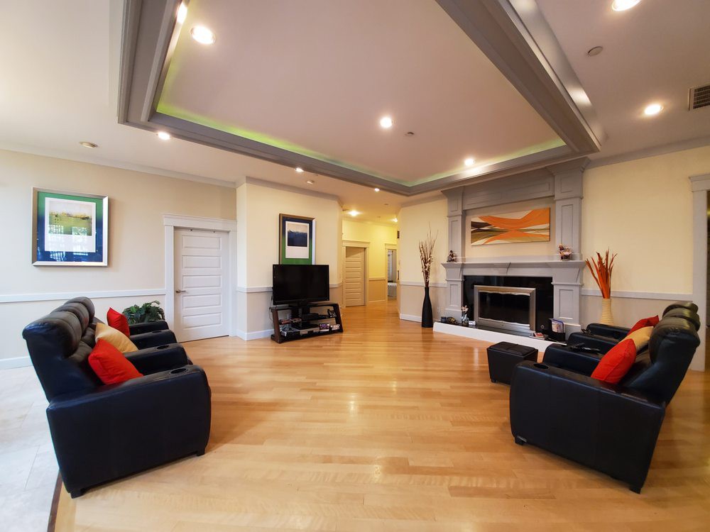 A spacious modern living room with hardwood flooring, featuring comfortable sofas, a fireplace, and a television, accented by contemporary artwork.