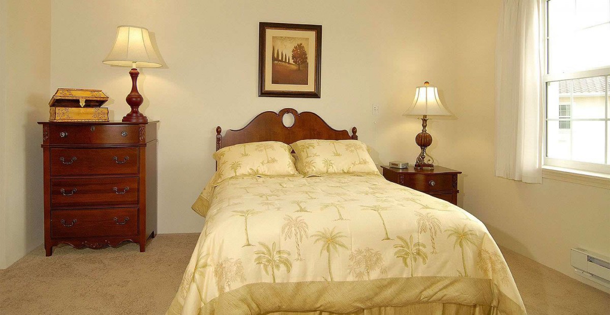 A cozy bedroom with a neatly made bed, flanked by bedside tables and lamps, adorned with a framed painting on the wall.