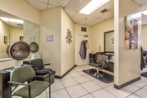 A cozy salon interior with chairs, a mirror, hair dryers, and a small waiting area.