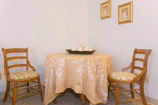 A cozy dining setup featuring a round table with an elegant tablecloth, accompanied by two wooden chairs and decorative wall art.