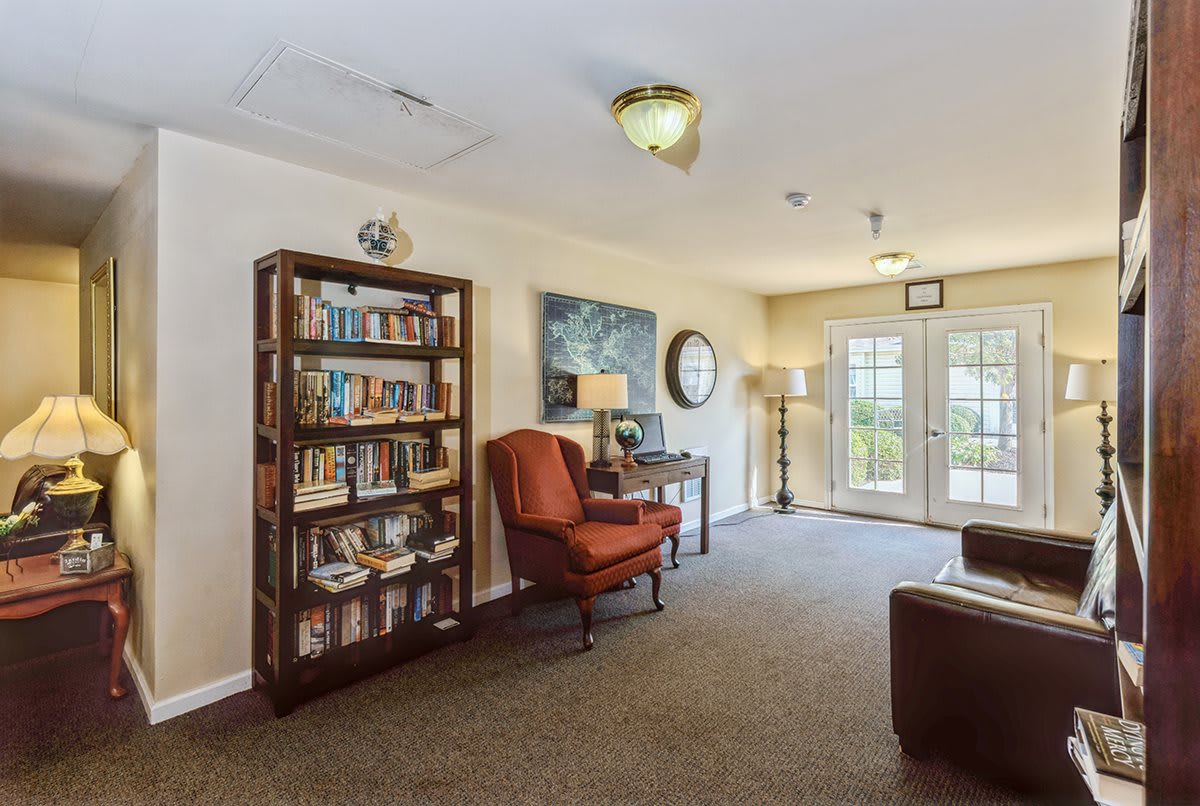 A cozy living room with a bookshelf, armchair, and natural light from the windows.