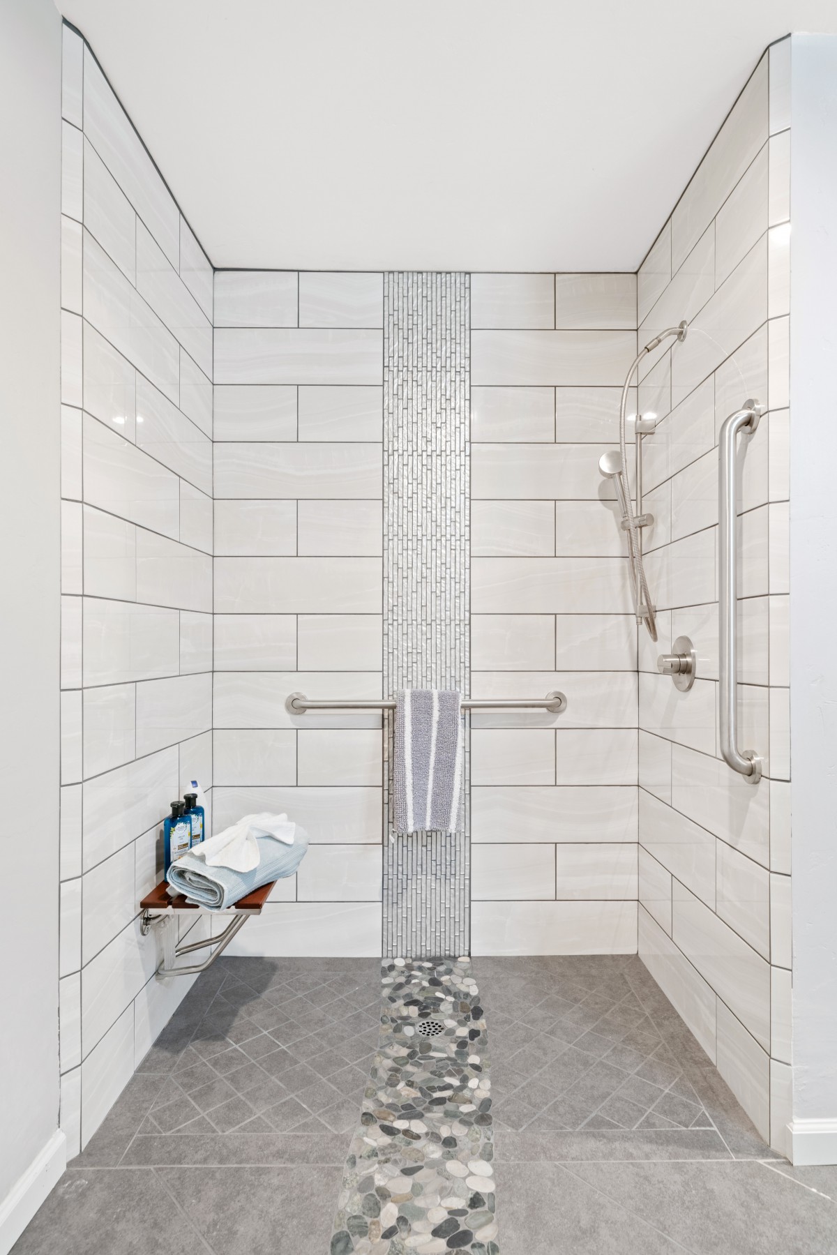 A modern, accessible shower featuring white tiles, a grab bar, and a bench.