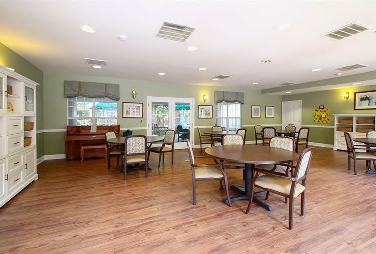A spacious dining room with several tables and chairs, featuring wooden flooring and decorated walls.