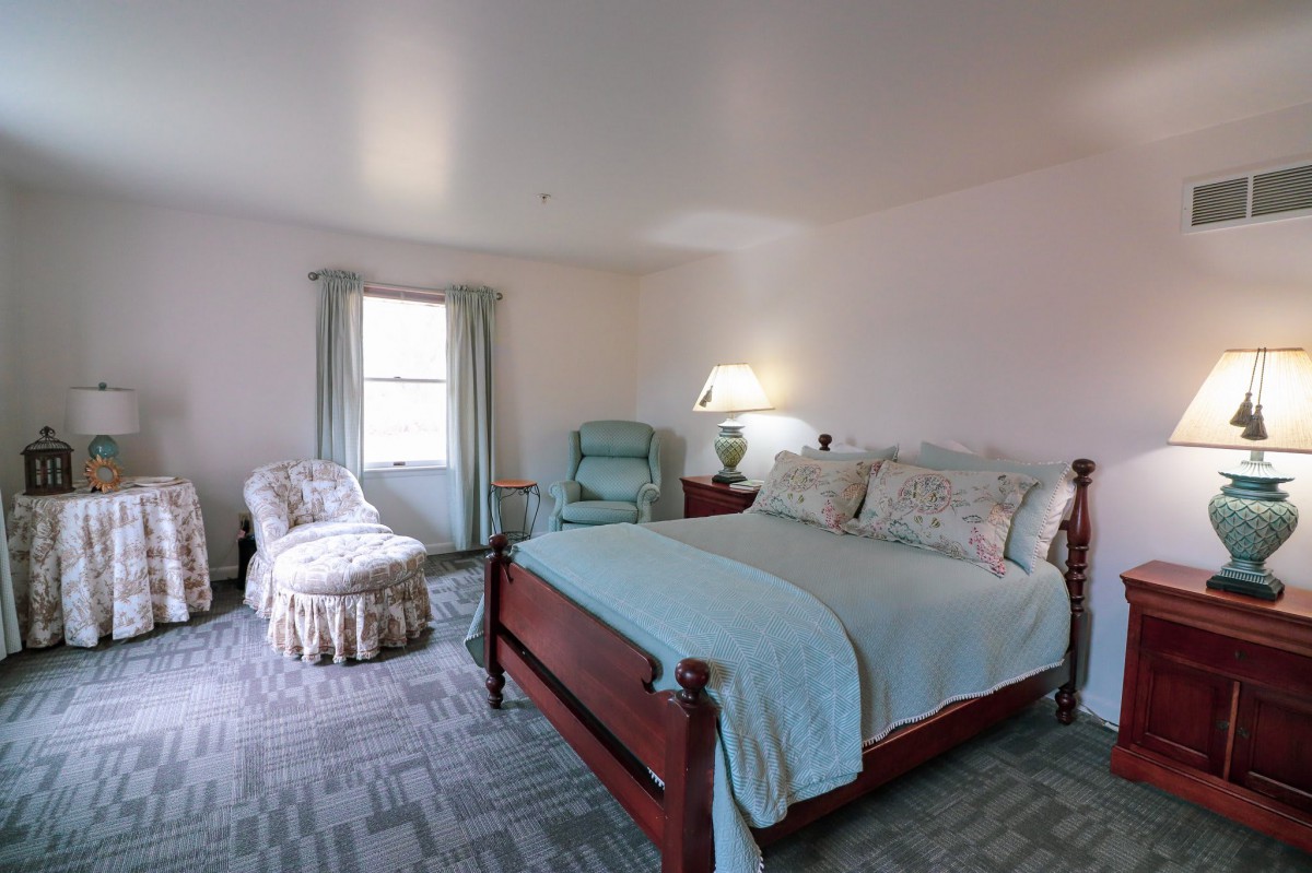A cozy bedroom featuring a large wooden bed, an armchair, and a lamp.