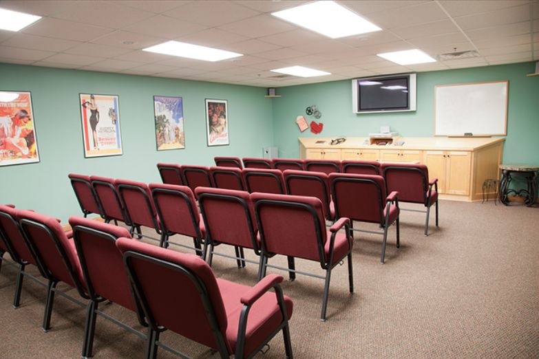 A small lecture room with rows of red chairs facing a presentation area.